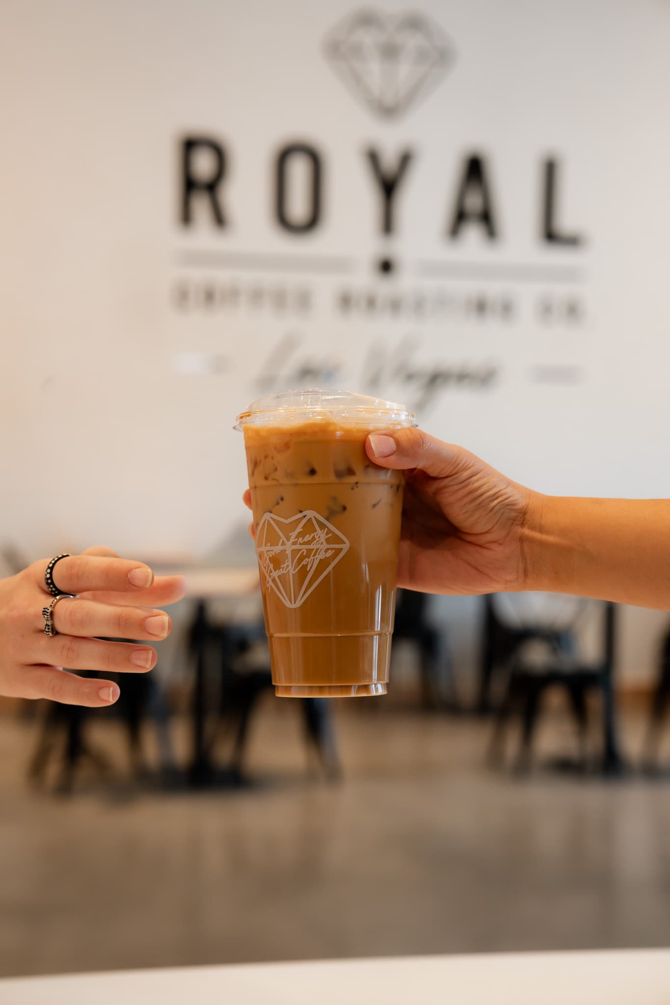 Iced caramel latte held up in front of the Royal logo wall