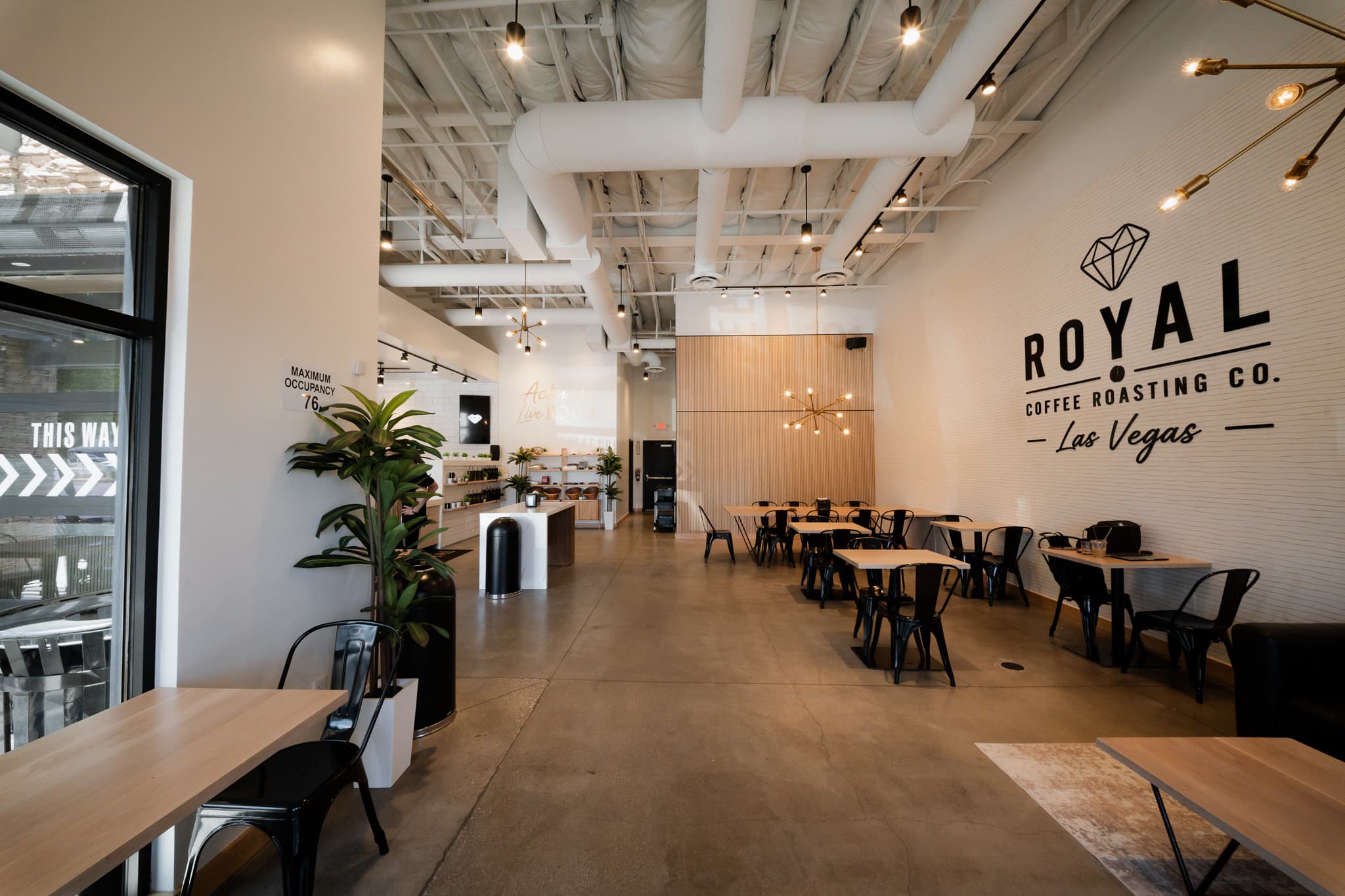 Inside Royal Coffee Roasting Co. in Las Vegas — wood tables, black chairs, and the Royal diamond logo wall